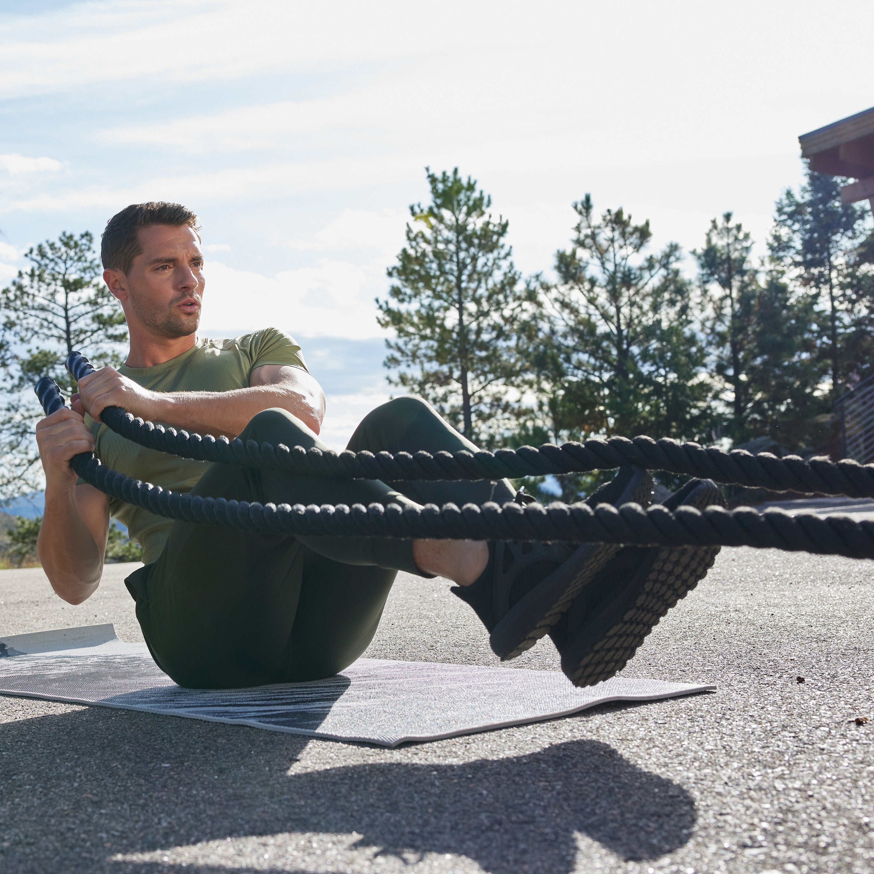 Person seated on a Yoga Mat in Boat Pose with the Conditioning Rope in each hand